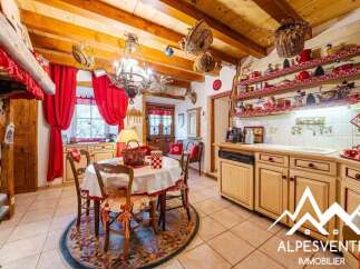 Charming rustic kitchen and dining area featuring exposed wooden beams, a traditional chandelier, and vibrant red curtains.