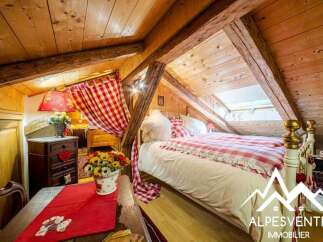 Charming attic bedroom featuring a cozy bed with red and white checkered bedding, complemented by rustic wooden beams and a sloped ceiling.