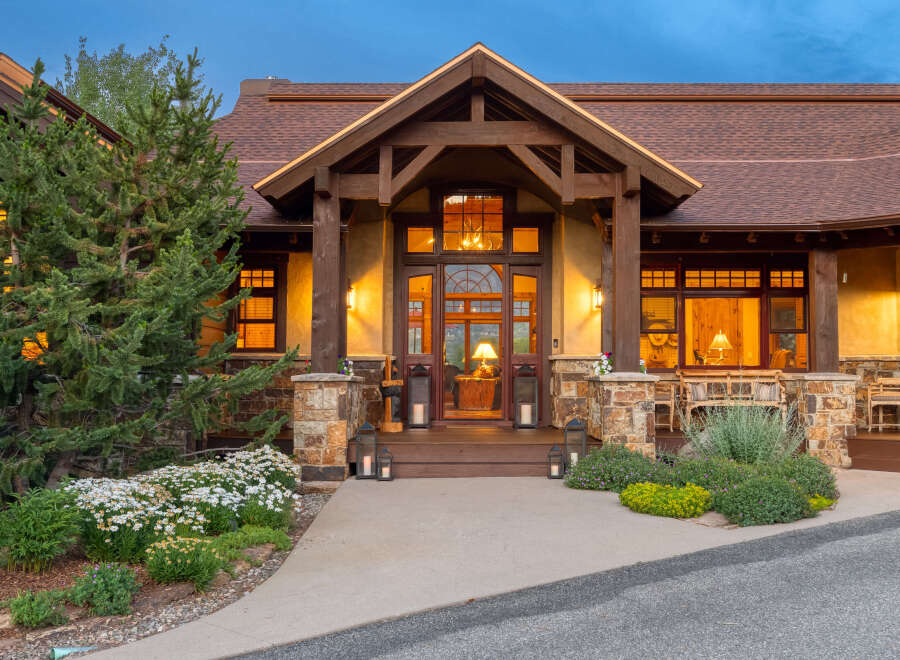 Experience luxury mountain living in this stunning lodge-style home, featuring a grand entrance with a rustic wooden door and arched glass.