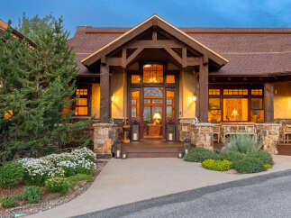 Experience luxury mountain living in this stunning lodge-style home, featuring a grand entrance with a rustic wooden door and arched glass.