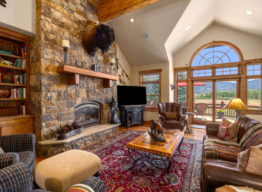 Experience rustic luxury in this stunning living room, featuring a grand stone fireplace and a magnificent bison head mount.