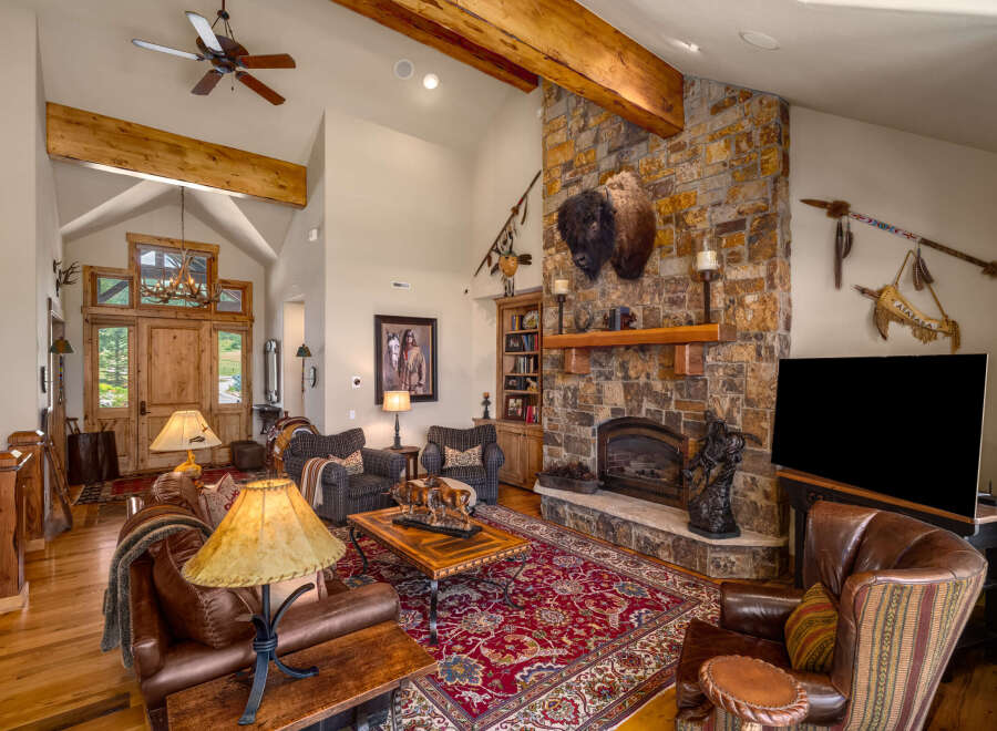Experience rustic elegance in this spacious living room, featuring a grand stone fireplace adorned with a majestic bison head and Native American artifacts.