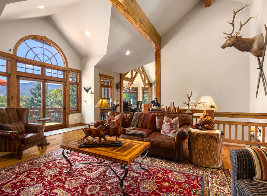 Experience rustic elegance in this spacious living room, featuring a grand arched window with stunning mountain views and exposed wooden beams.