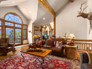 Experience rustic elegance in this spacious living room, featuring a grand arched window with stunning mountain views and exposed wooden beams.