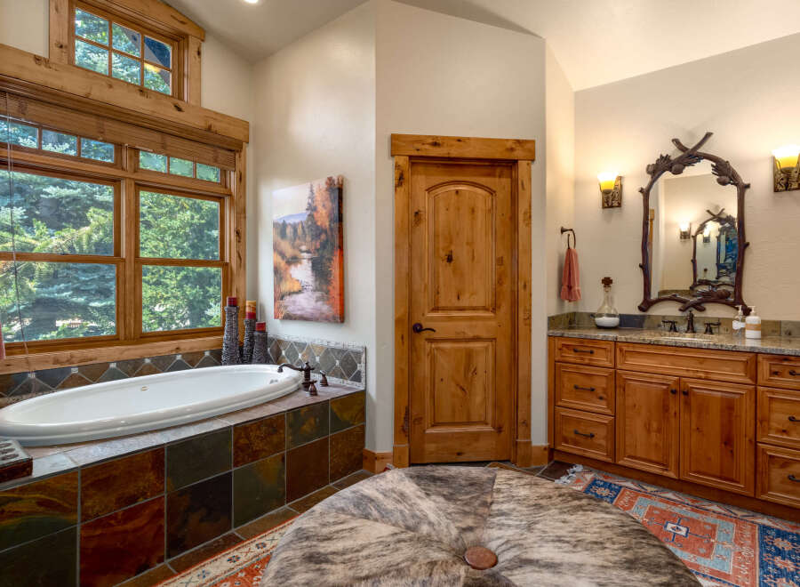 Indulge in relaxation in this luxurious bathroom featuring a deep soaking tub with stunning forest views through large wooden-framed windows.