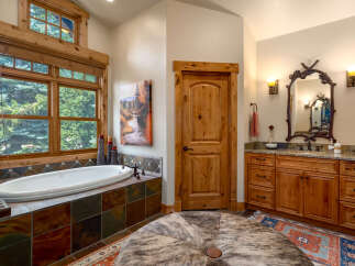 Indulge in relaxation in this luxurious bathroom featuring a deep soaking tub with stunning forest views through large wooden-framed windows.