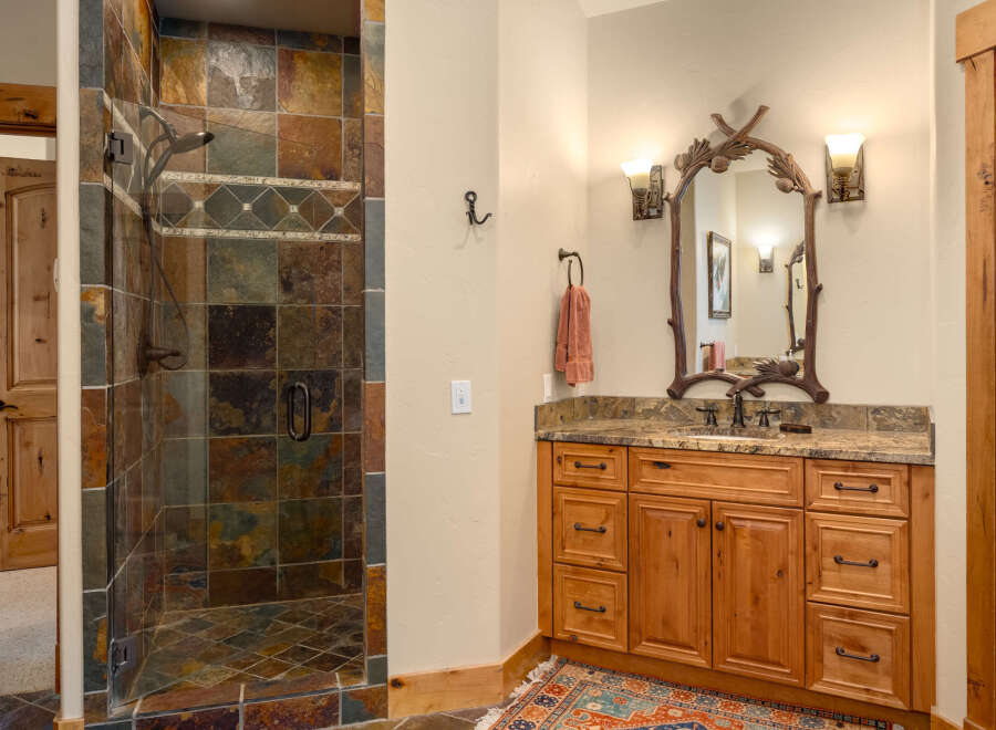 This rustic bathroom features a spacious walk-in shower with multi-colored slate tile and a decorative accent band.