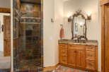 This rustic bathroom features a spacious walk-in shower with multi-colored slate tile and a decorative accent band.