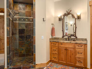 This rustic bathroom features a spacious walk-in shower with multi-colored slate tile and a decorative accent band.