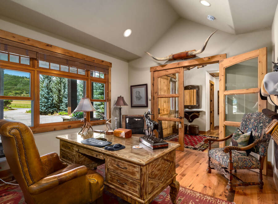 This rustic office space features a large wooden desk with a leather chair and a decorative rug.