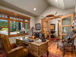 This rustic office space features a large wooden desk with a leather chair and a decorative rug.