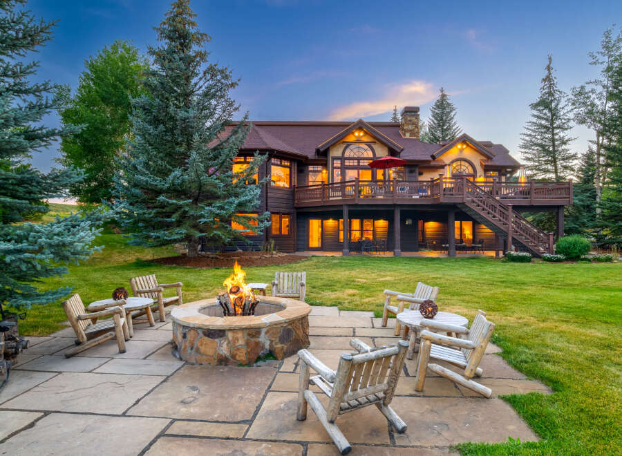 Experience the ultimate mountain retreat with this stunning property, featuring a spacious backyard with a stone fire pit and comfortable log seating, perfect for evening gatherings.