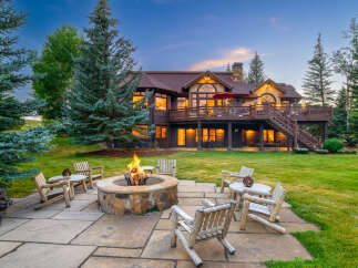 Experience the ultimate mountain retreat with this stunning property, featuring a spacious backyard with a stone fire pit and comfortable log seating, perfect for evening gatherings.