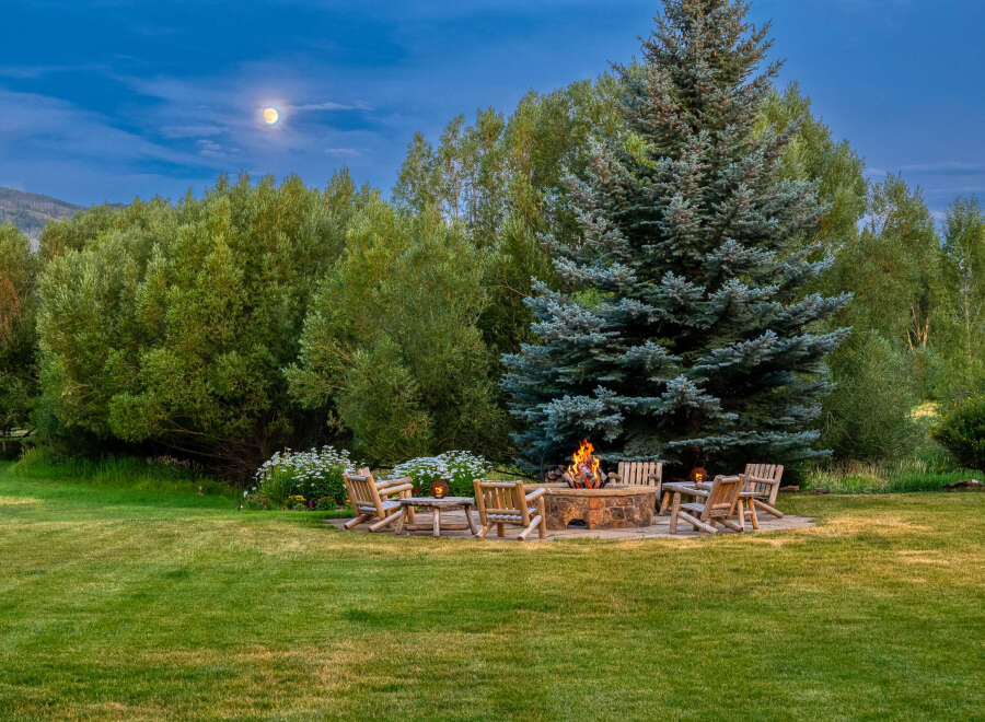 Experience the magic of twilight with this stunning outdoor living space, featuring a stone fire pit surrounded by comfortable Adirondack chairs, perfect for gathering under the moonlight.