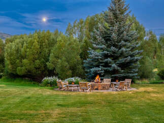 Experience the magic of twilight with this stunning outdoor living space, featuring a stone fire pit surrounded by comfortable Adirondack chairs, perfect for gathering under the moonlight.