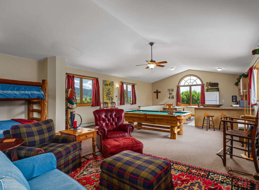 Experience ultimate relaxation and entertainment in this spacious game room, featuring a full-size pool table and a cozy seating area with a plush red leather armchair and ottoman.