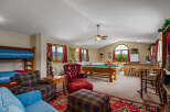 Experience ultimate relaxation and entertainment in this spacious game room, featuring a full-size pool table and a cozy seating area with a plush red leather armchair and ottoman.