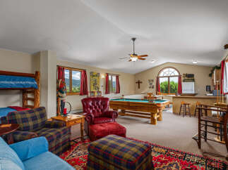 Experience ultimate relaxation and entertainment in this spacious game room, featuring a full-size pool table and a cozy seating area with a plush red leather armchair and ottoman.