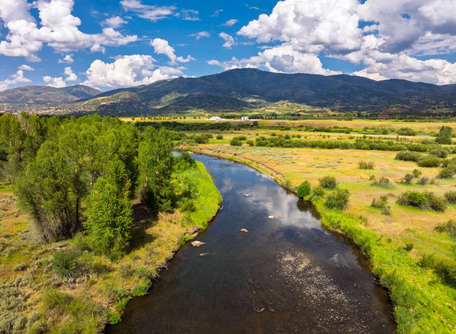 Experience the serene beauty of this expansive landscape, featuring a meandering river that flows through lush green banks and golden meadows.