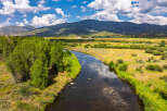 Experience the serene beauty of this expansive landscape, featuring a meandering river that flows through lush green banks and golden meadows.