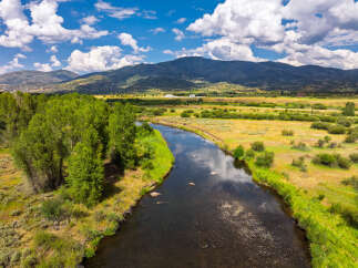 Experience the serene beauty of this expansive landscape, featuring a meandering river that flows through lush green banks and golden meadows.