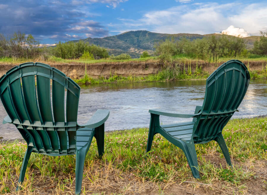 Enjoy serene riverfront living with this stunning property, featuring two Adirondack chairs perfectly positioned for breathtaking views.