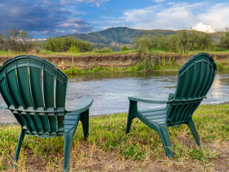 Enjoy serene riverfront living with this stunning property, featuring two Adirondack chairs perfectly positioned for breathtaking views.