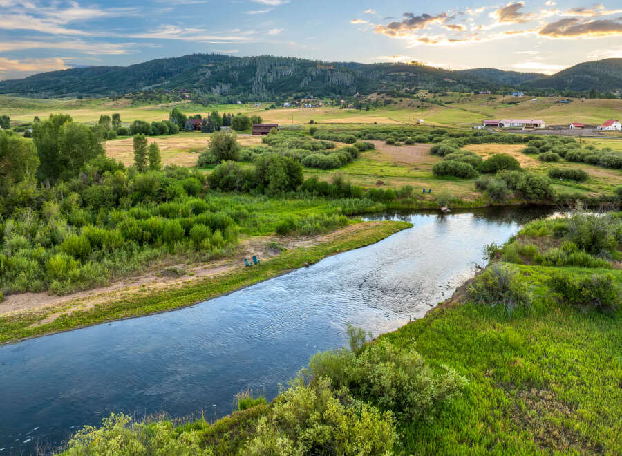 Discover your dream home nestled in a picturesque landscape, offering a serene riverfront setting with lush greenery and rolling hills.