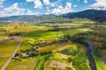 Experience the serene beauty of this expansive rural landscape, featuring a winding river, lush green fields, and majestic mountains in the distance.