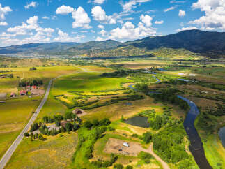 Experience the serene beauty of this expansive rural landscape, featuring a winding river, lush green fields, and majestic mountains in the distance.