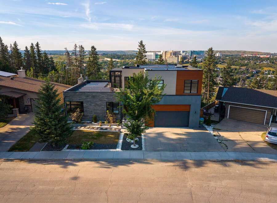 Experience modern luxury in this stunning multi-level home featuring a sleek stone facade, expansive windows, and a flat roof with solar panels.