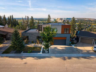Experience modern luxury in this stunning multi-level home featuring a sleek stone facade, expansive windows, and a flat roof with solar panels.