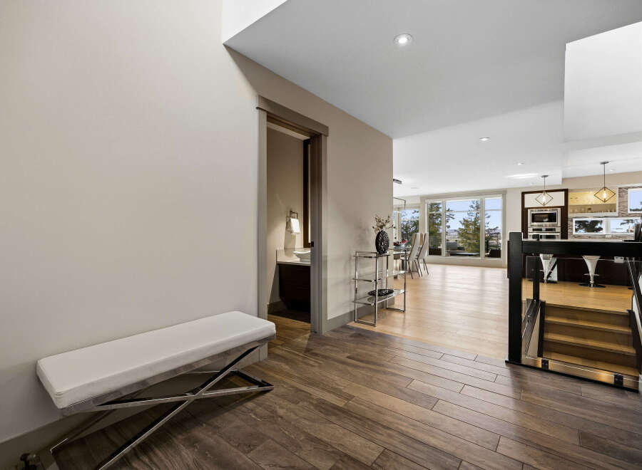 Step into this modern entryway featuring a sleek white bench and rich wood-look tile flooring.