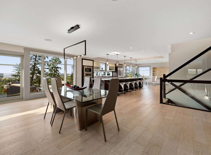 Experience modern luxury in this open-concept living space, featuring a sleek dining area with a glass table and contemporary chairs, seamlessly flowing into a gourmet kitchen with a large island and bar seating.