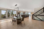 Experience modern luxury in this open-concept living space, featuring a sleek dining area with a glass table and contemporary chairs, seamlessly flowing into a gourmet kitchen with a large island and bar seating.
