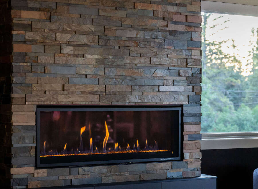 Experience modern luxury with this stunning fireplace, featuring a stacked stone facade and a sleek, linear gas insert.