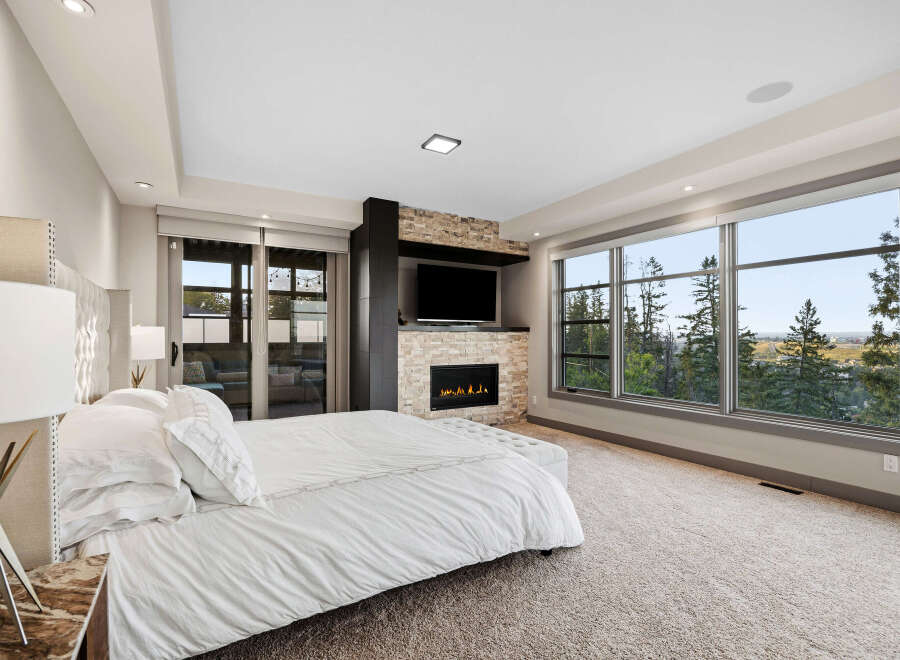 Experience luxury living in this master bedroom, featuring a cozy fireplace and a large TV for ultimate relaxation.