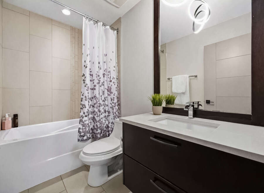 This modern bathroom features a sleek white bathtub with a decorative shower curtain, complemented by a clean-lined toilet.