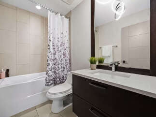 This modern bathroom features a sleek white bathtub with a decorative shower curtain, complemented by a clean-lined toilet.