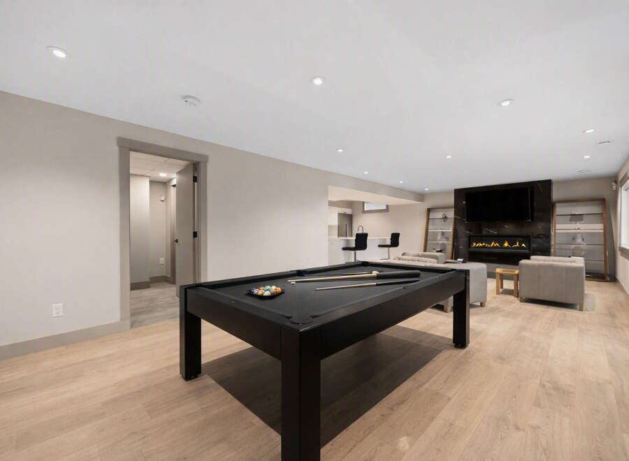 This modern basement features a sleek black pool table as the centerpiece, perfect for entertainment.