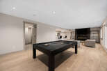 This modern basement features a sleek black pool table as the centerpiece, perfect for entertainment.