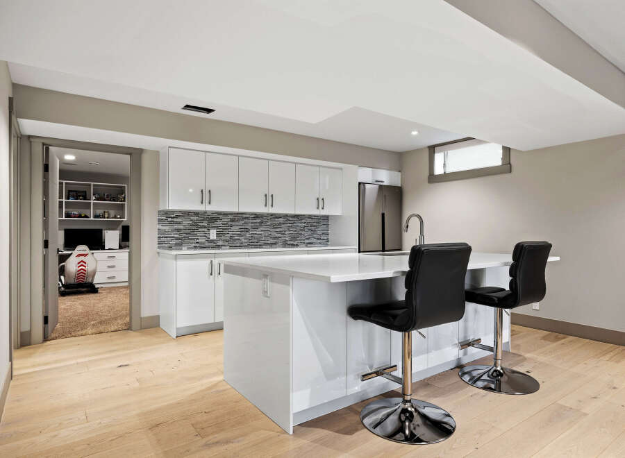 Discover modern living in this stunning basement suite, featuring a sleek, high-gloss white kitchen with a captivating mosaic tile backsplash.