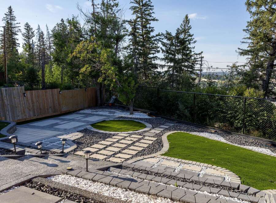 Discover this beautifully landscaped backyard, featuring a modern patio with intricate paving stone patterns and contrasting white and dark gravel accents.