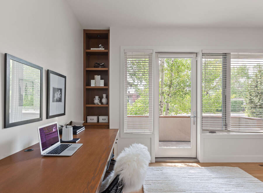 This home office features a sleek wooden desk with a laptop and a fluffy white chair, perfect for productive work sessions.