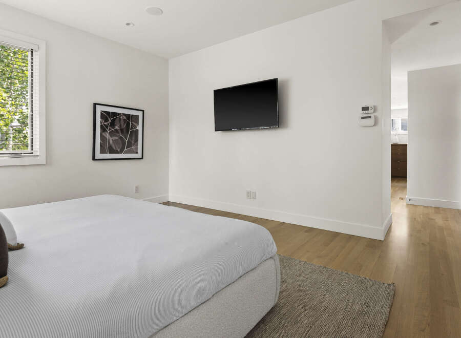 This modern bedroom features a comfortable bed with striped bedding, a wall-mounted television, and a large window with blinds offering natural light.