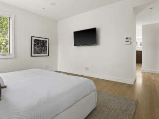 This modern bedroom features a comfortable bed with striped bedding, a wall-mounted television, and a large window with blinds offering natural light.
