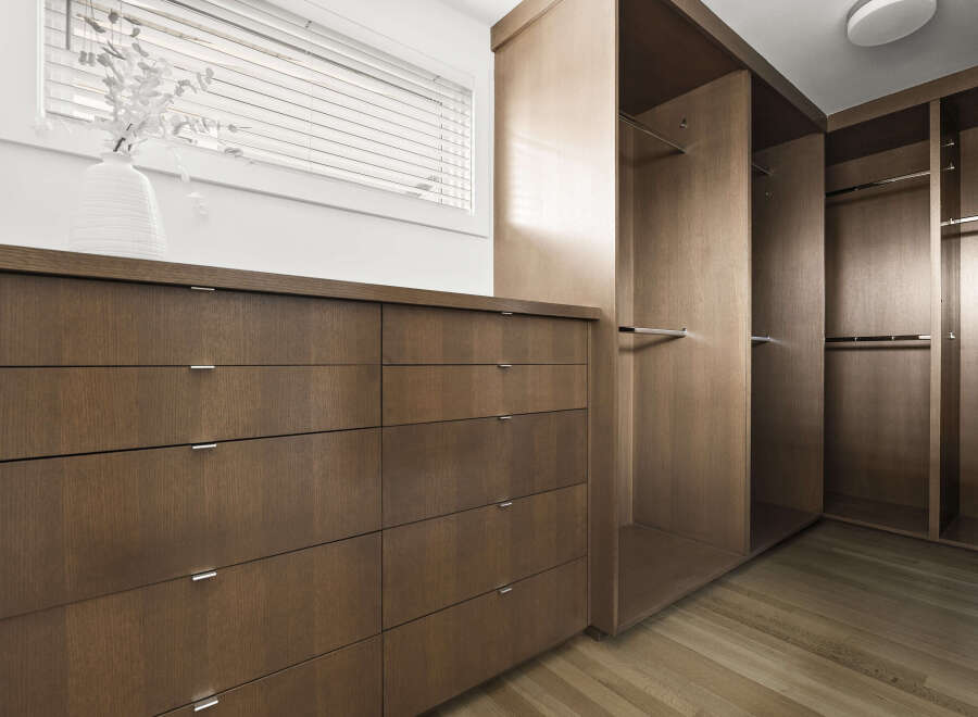 Discover ample storage solutions in this modern walk-in closet, featuring a sleek dresser with multiple drawers and built-in shelving with hanging rods.