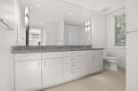This modern bathroom features a sleek white vanity with a granite countertop and dual sinks, complemented by a large mirror reflecting a tiled shower.