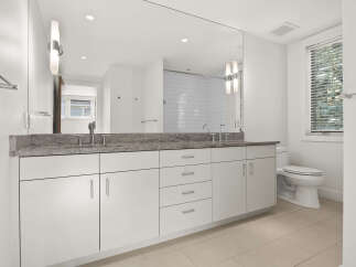 This modern bathroom features a sleek white vanity with a granite countertop and dual sinks, complemented by a large mirror reflecting a tiled shower.
