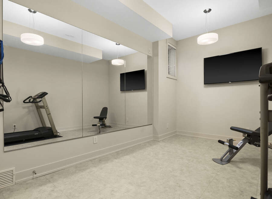 This home gym features a spacious layout with a large mirror, a treadmill, and a weight bench, perfect for your fitness routine.